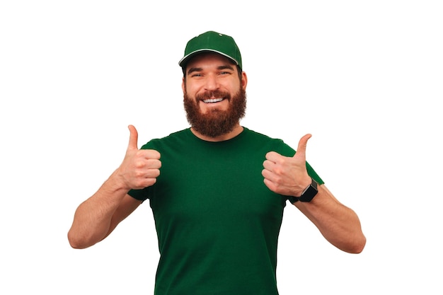 Przystojny uśmiechnięty dostawca ubrany w zielony mundur pokazuje dwa kciuki do góry