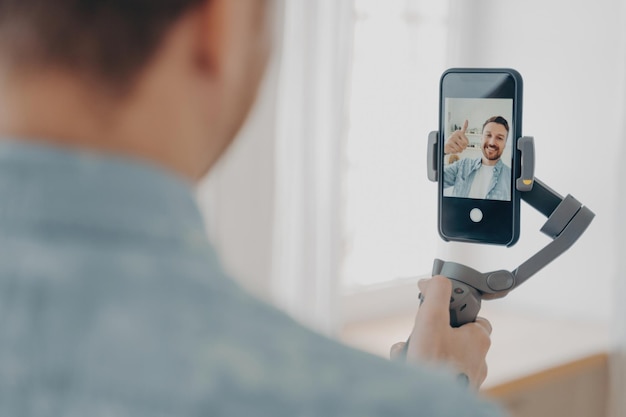 Przystojny uśmiechnięty młody brunete mężczyzna z zarostem robi selfie na smartfonie