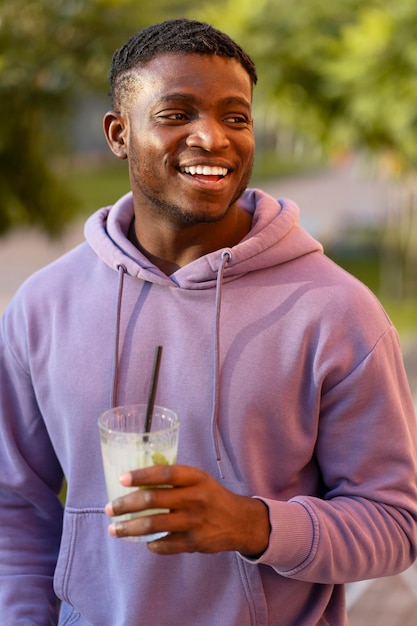 Przystojny, uśmiechnięty, stylowy Afroamerykanin, młody mężczyzna trzymający lemoniadę i odwracający wzrok na ulicy