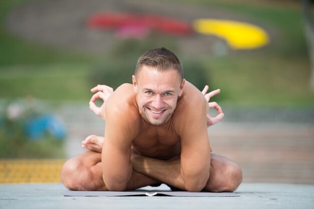 Przystojny wysportowany mężczyzna robi asany jogi w parku