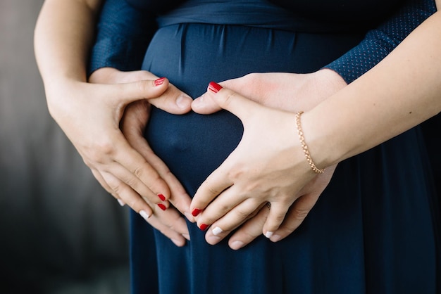 Przyszli rodzice trzymają ręce na brzuchu młodej kobiety w ciąży w kształcie serca