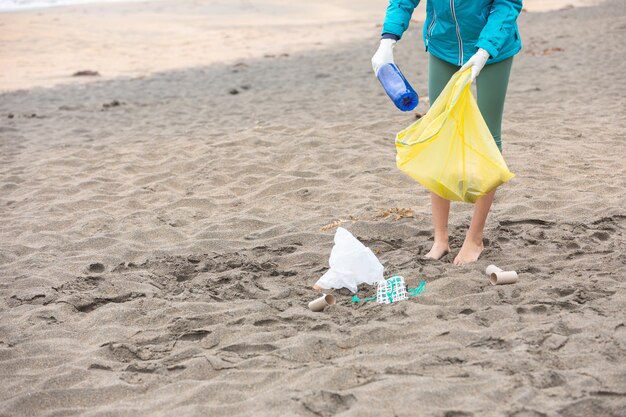 Przytnij nierozpoznawalną wolontariuszkę sprzątającą plażę ze śmieci