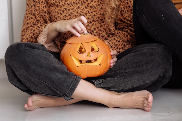 Przytnij widok dorosłej kobiety siedzącej w domu floorat z rzeźbionymi halloweenowymi dyniami z dyni jackolantern w pomieszczeniu Sztuczka lub tułów Happy Halloween day selektywne focus