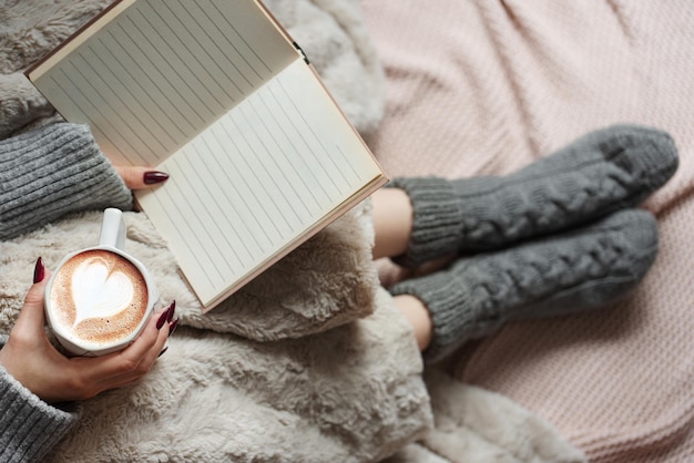 Przytulna domowa kobieta okryta ciepłym kocem pije kawę i stroi książkę