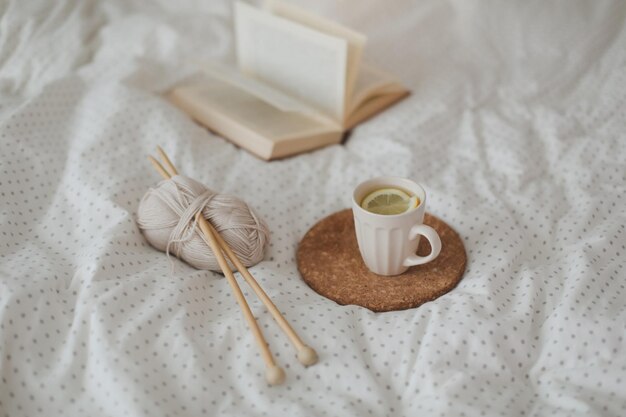 Przytulna zimowa kompozycja z książkową herbatą z cytryną i drutami na pościeli