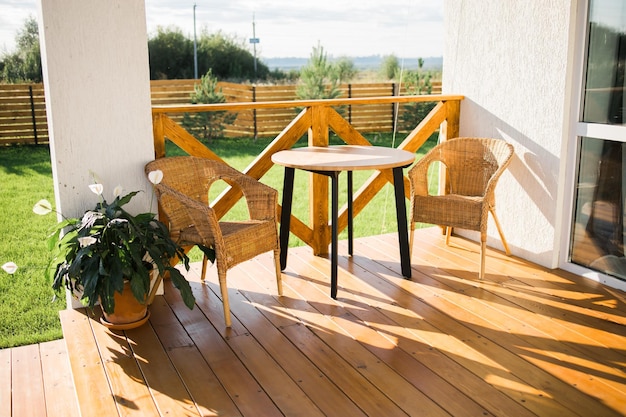 Przytulny drewniany taras wiejskiego domu lub domku ze stołem i krzesłem z widokiem na ogród na relaksujący wieczór