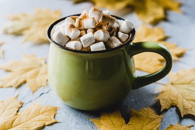 Przytulny jesienny gorący napój z pianką marshmallow i żółtymi liśćmi klonu