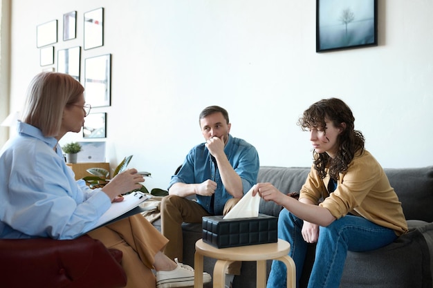 Psycholog rozmawia z parą na sesji, gdy siedzą na kanapie i słuchają jej
