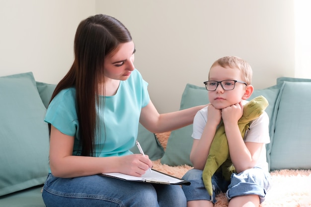 Psycholog słucha małego dziecka podczas sesji terapeutycznej. Przedszkolak czuje się swobodnie w gabinecie terapeuty, dzieli się swoimi przemyśleniami i problemami