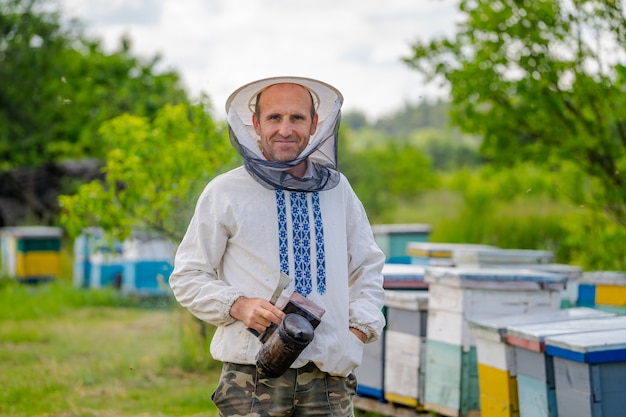 Pszczelarz w ochronnej odzieży roboczej. Tło uli w pasiece. Pracuje na pasiekach na wiosnę.