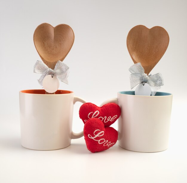 Zdjęcie puchar miłości, dwie filiżanki kawy z ikoną czerwonego serca i drewnianą łyżką na białym tle