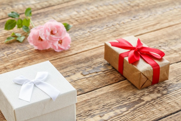 Pudełka na prezenty owinięte wstążkami na starych drewnianych deskach ozdobionych różowymi różami. Widok z góry.