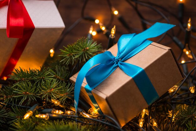 Pudełka na prezenty świąteczne z czerwonymi i niebieskimi kokardkami i światłami na drewnianej powierzchni