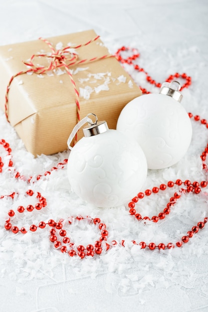 Pudełka na prezenty świąteczne z papieru pakowego, czerwonych koralików, białych bombek i gałęzi jodłowych na pokrytym śniegiem stole
