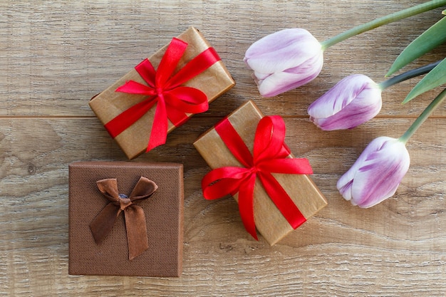 Pudełka na prezenty z czerwonymi wstążkami i pięknymi liliowymi tulipanami Koncepcja dawania prezentu na święta