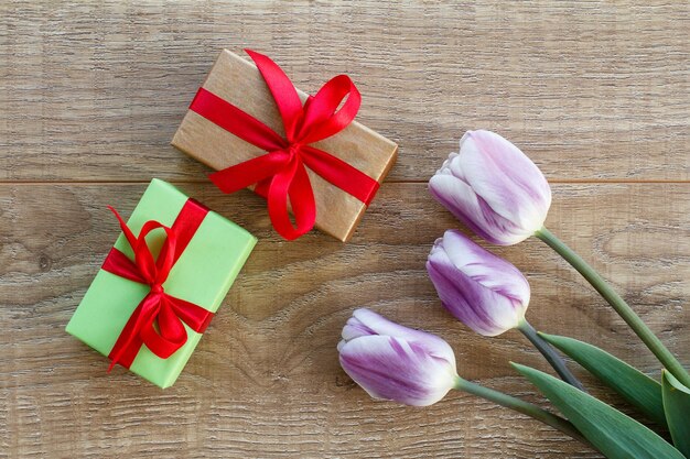 Pudełka na prezenty z czerwonymi wstążkami i pięknymi tulipanami na drewnianych deskach