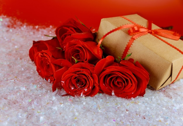 Zdjęcie pudełko i bukiet pięknych czerwonych róż na błyszczącym śniegu. koncepcja na dzień matki lub walentynki.