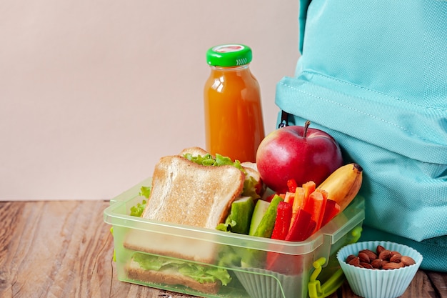 Pudełko Na Lunch Z Apetycznym Jedzeniem I Plecakiem Na Drewnianym Stole.