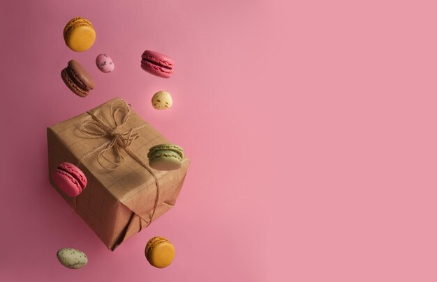 Pudełko na prezent i lewitujące słodycze macarons i cukierki na różowym tle miejsca na kopię