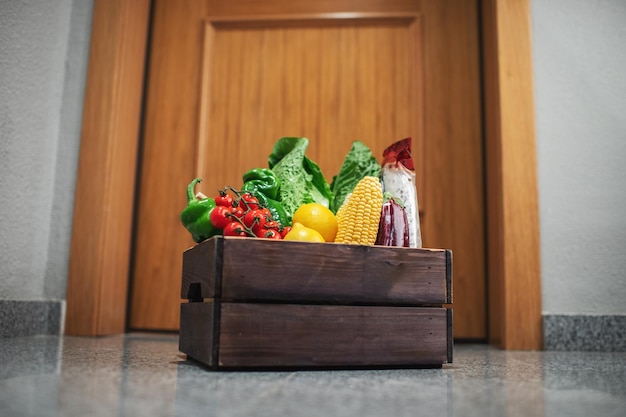 Pudełko na zakupy spożywcze stoi przy drzwiach domu lub mieszkania. Dostawa warzyw i owoców podczas kwarantanny i samoizolacji