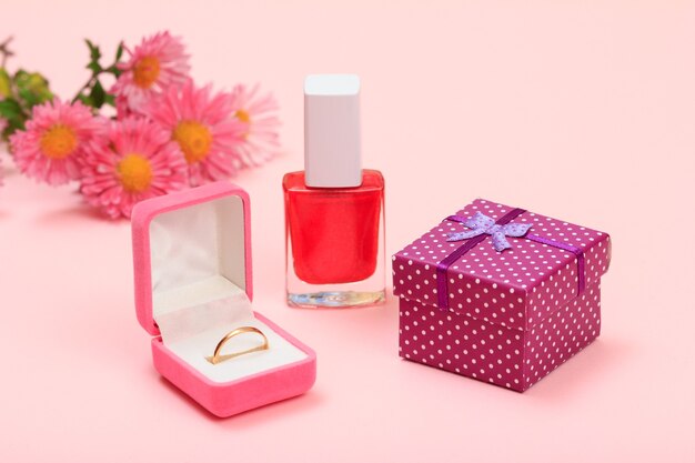 Pudełko prezentowe, butelka z lakierem do paznokci, złoty pierścionek w pudełku i kwiaty na różowym tle. Kosmetyki i akcesoria dla kobiet.