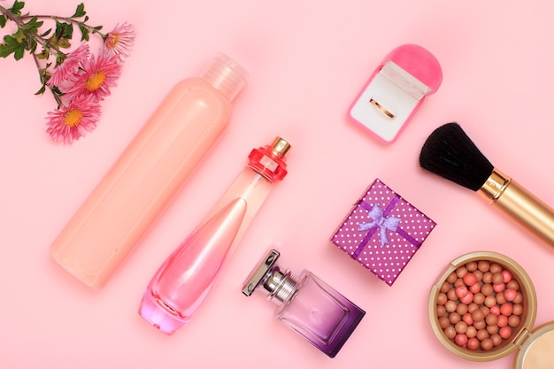 Pudełko prezentowe, butelki perfum, szampon i złoty pierścionek w pudełku, proszek z pędzlem na różowym tle. Kosmetyki i akcesoria dla kobiet. Widok z góry.