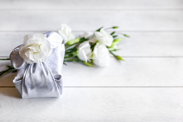 Pudełko prezentowe modne owinięte jedwabną tkaniną w technice Furoshiki biały kwiat Eustoma lub Lisianthus drewniane tło Zero Waste Life Concept