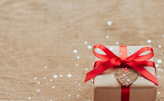 Pudełko prezentowe owinięte w brązowy papier z czerwoną kokardą, posypane srebrnymi cekinami w kształcie gwiazdy, kopia przestrzeń, prezent na Boże Narodzenie