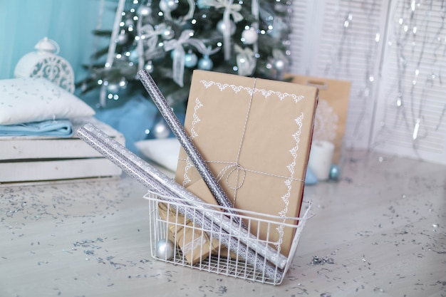 Pudełko świąteczne z prezentem przewiązanym wstążką na tle choinki.