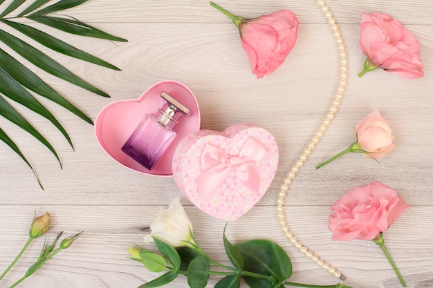 Pudełko w kształcie serca z butelką perfum oraz różowymi kwiatami i zielonymi liśćmi.