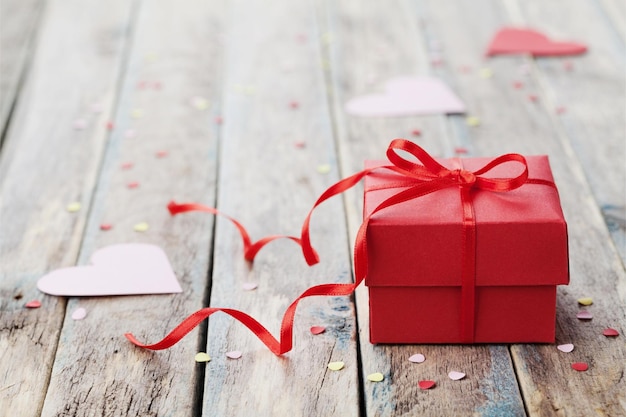 Pudełko z czerwoną kokardką i papierowym sercem na drewnianym stole na Walentynki