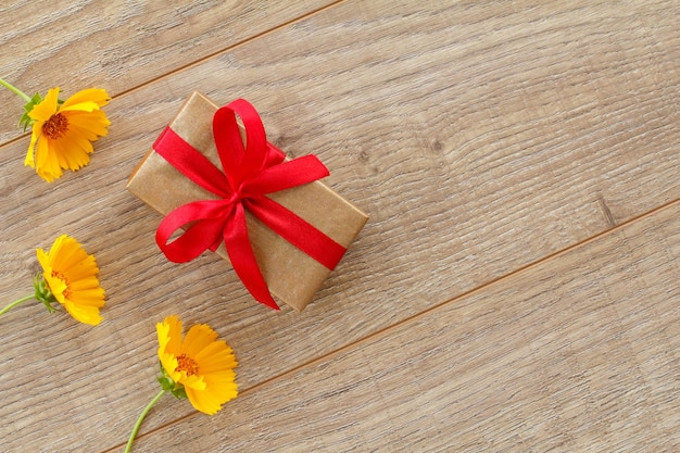 Pudełko z czerwonymi wstążkami i pięknymi kwiatami rumianku na drewnianym tle. Koncepcja dawania prezentu na święta. Widok z góry z miejscem na kopię.