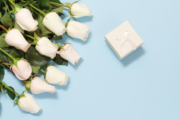Pudełko z pięknymi białymi różami na niebieskim tle. Koncepcja dawania prezentu na święta. Widok z góry.