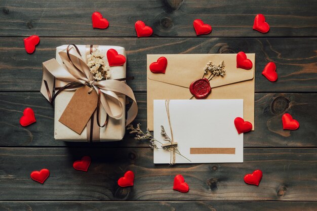 Zdjęcie pudełko z prezentami i kartką z wstążką łukową i papierowymi sercami na drewnianym stole na święto walentynek