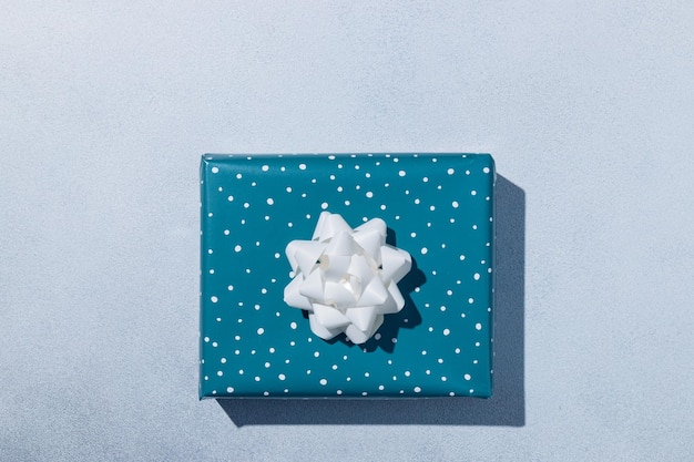 Pudełko zawinięte w niebieski papier z białą kokardką na szarym tle Koncepcja kartki świątecznej Makieta