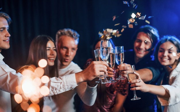 Pukające okulary. Grupa wesołych przyjaciół z okazji Nowego Roku w pomieszczeniu z napojami w rękach.