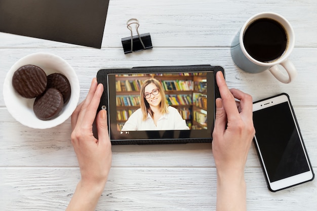 Zdjęcie pulpit z tabletem, telefonem, kawą i ciasteczkami, widok z góry. kobieta ogląda film edukacyjny