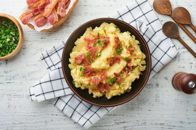 Puree ziemniaczane Puree ziemniaczane bekonowe z zieloną cebulą, pieprzem i serem cheddar w misce na starych drewnianych tłach Pyszne kremowe puree ziemniaczane Widok z góry