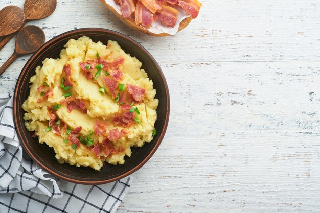 Puree ziemniaczane Puree ziemniaczane bekonowe z zieloną cebulą, pieprzem i serem cheddar w misce na starych drewnianych tłach Pyszne kremowe puree ziemniaczane Widok z góry