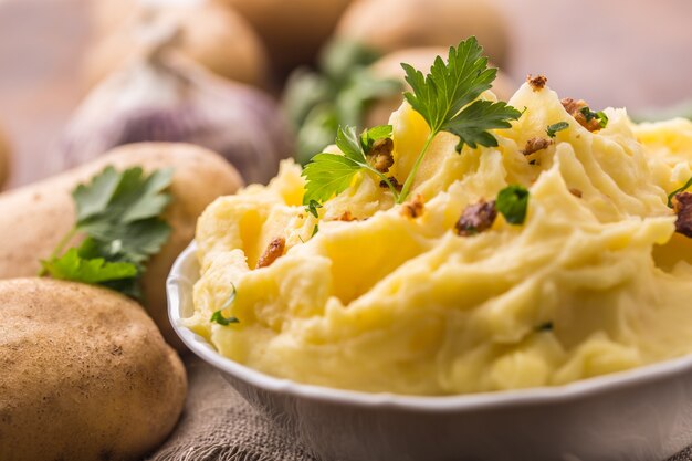 Puree ziemniaczane w misce udekorowane natką pietruszki i pieczonymi kawałkami boczku.