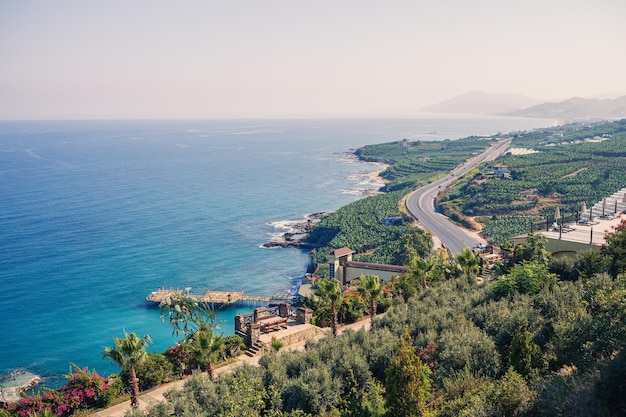 Pusta asfaltowa droga wije się wzdłuż zapierającego dech w piersiach malowniczego wybrzeża w słoneczny letni dzień Spektakularne ujęcie nadmorskiej drogi z widokiem na czyste, błękitne niebo i spokojne Morze Śródziemne