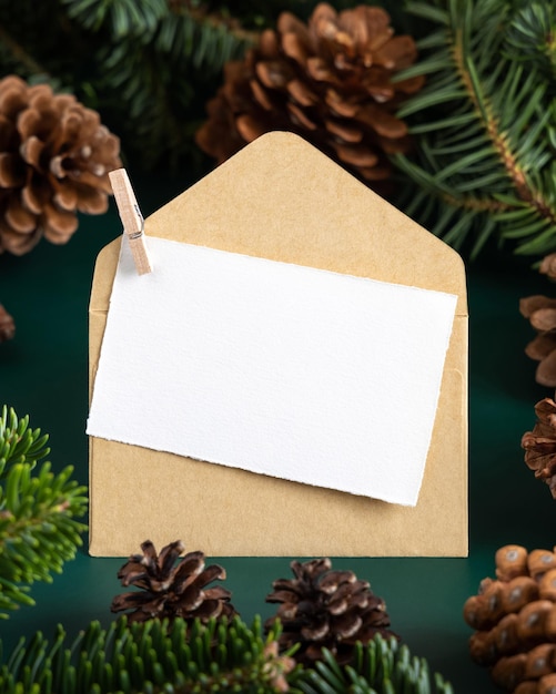 Pusta kartka świąteczna i koperta między gałęziami jodły i szyszkami na zielonym zbliżeniu
