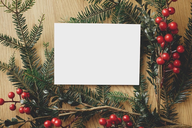 Zdjęcie pusta kartka z pozdrowieniami i gałęzie sosny z czerwonymi jagodami na drewnianym stole karta świąteczna z makietą płaskiego układu przestrzeń na tekst szablon kartki pocztowej z pozdrawieniami sezonowymi