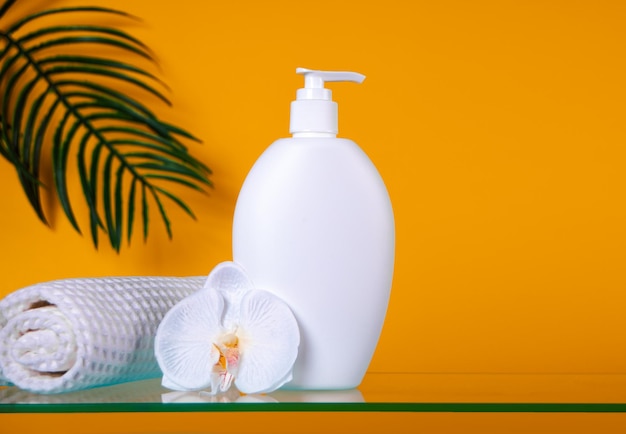 Pusta makieta butelki kosmetyk kosmetyczny do pielęgnacji skóry produkt organiczny do kąpieli z ręcznikiem z liści palmowych i orchidei kwiatowej na pomarańczowym tle Umieść swój projekt