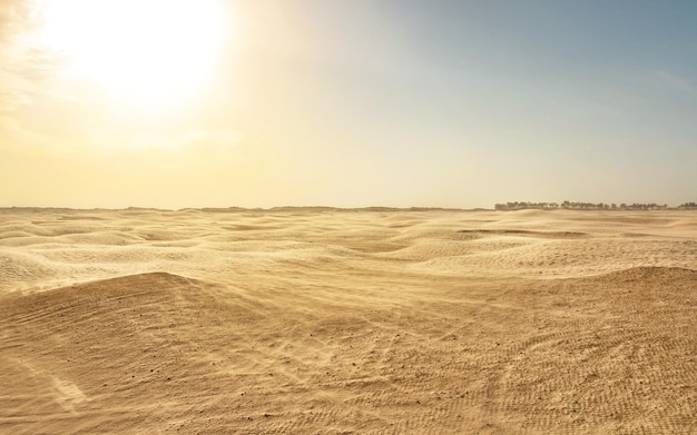 Pusta płaska pustynia sahara, wiatr tworzący pył piaskowy, z podświetleniem słońca w tle. Douz, Tunezja