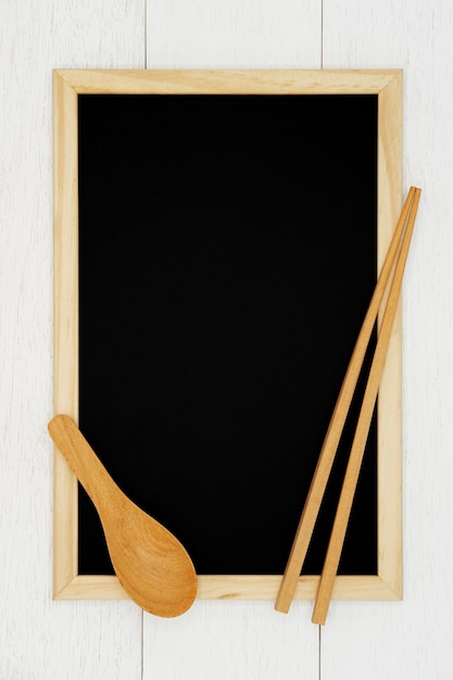 Pusta tablica z drewnianą łyżką i pałeczkami na białym tle drewnianej deski