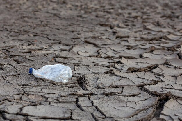 Pusta zmięta plastikowa butelka na suchej popękanej pustyni błotnej jak szare tło