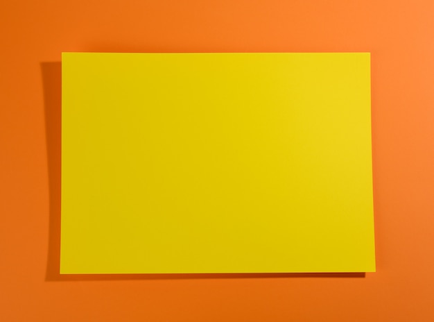 Pusta żółta kartka papieru na pomarańczowej powierzchni z cieniem, abstrakcyjne tło dla napisu, miejsce kopiowania
