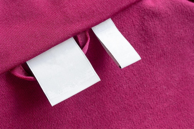 Puste białe pranie odzieży pielęgnacyjnej etykiety na tle tekstury czerwonej tkaniny