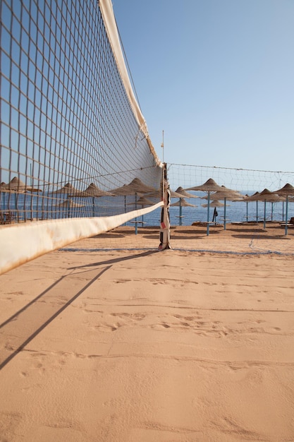 Zdjęcie puste boisko do siatkówki plażowej na żółtym piasku na tle parasoli i morza
